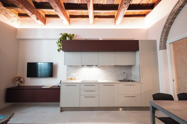 A modern kitchen with white cabinets, a marble backsplash, and a wooden ceiling.