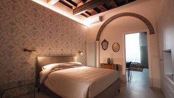 A bedroom with a bed, a nightstand, a dresser, a mirror, and an arched doorway leading to another room.