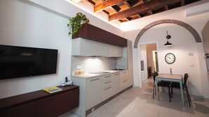 Cozinha moderna com televisão de tela plana, área de jantar com mesa e cadeiras, e um relógio na parede.