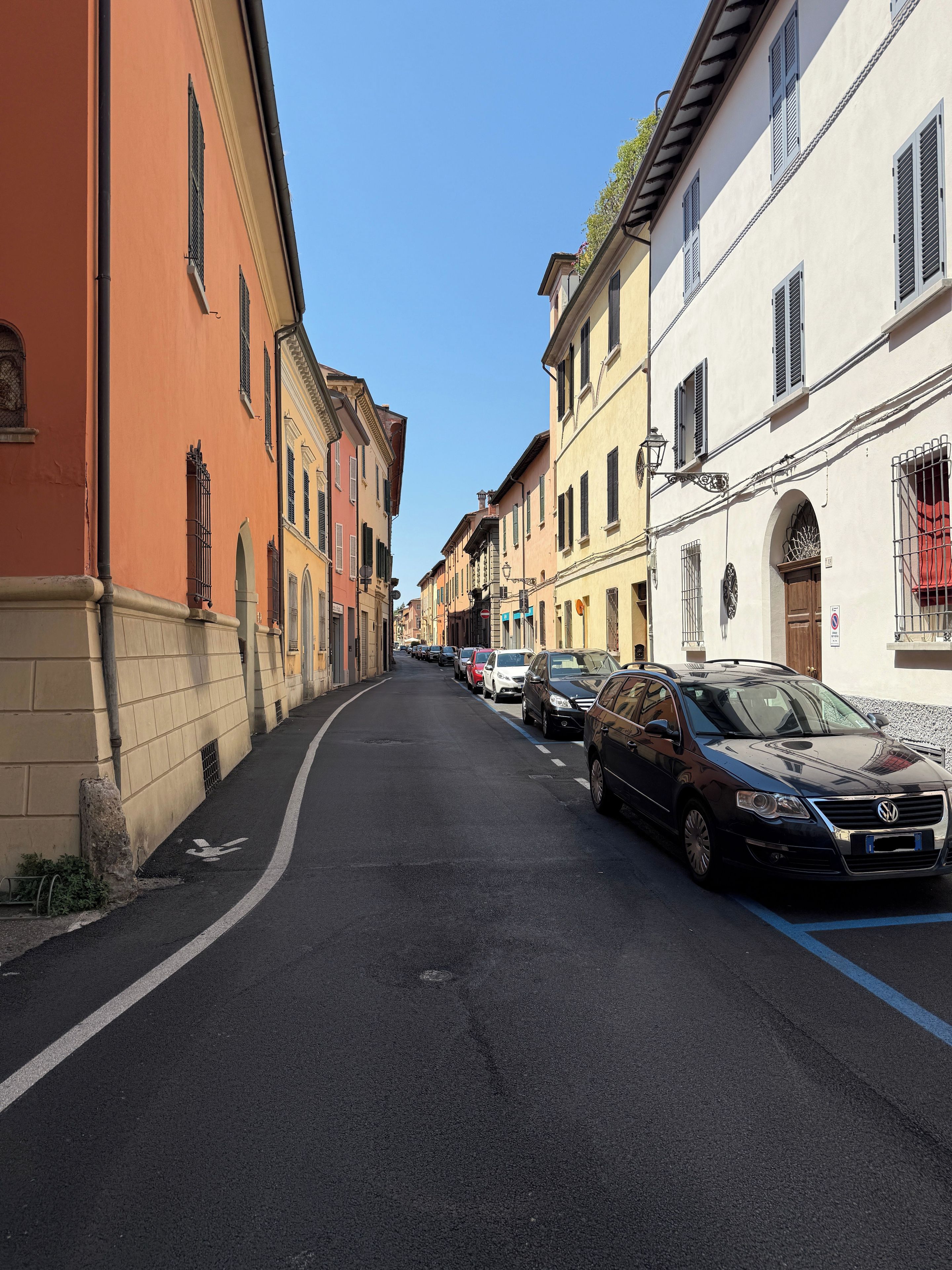 Eine schmale Straße, gesäumt von parkenden Autos und historischen Gebäuden.