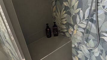 Zona doccia con porta in vetro, soffione e due flaconi di shampoo su un ripiano.