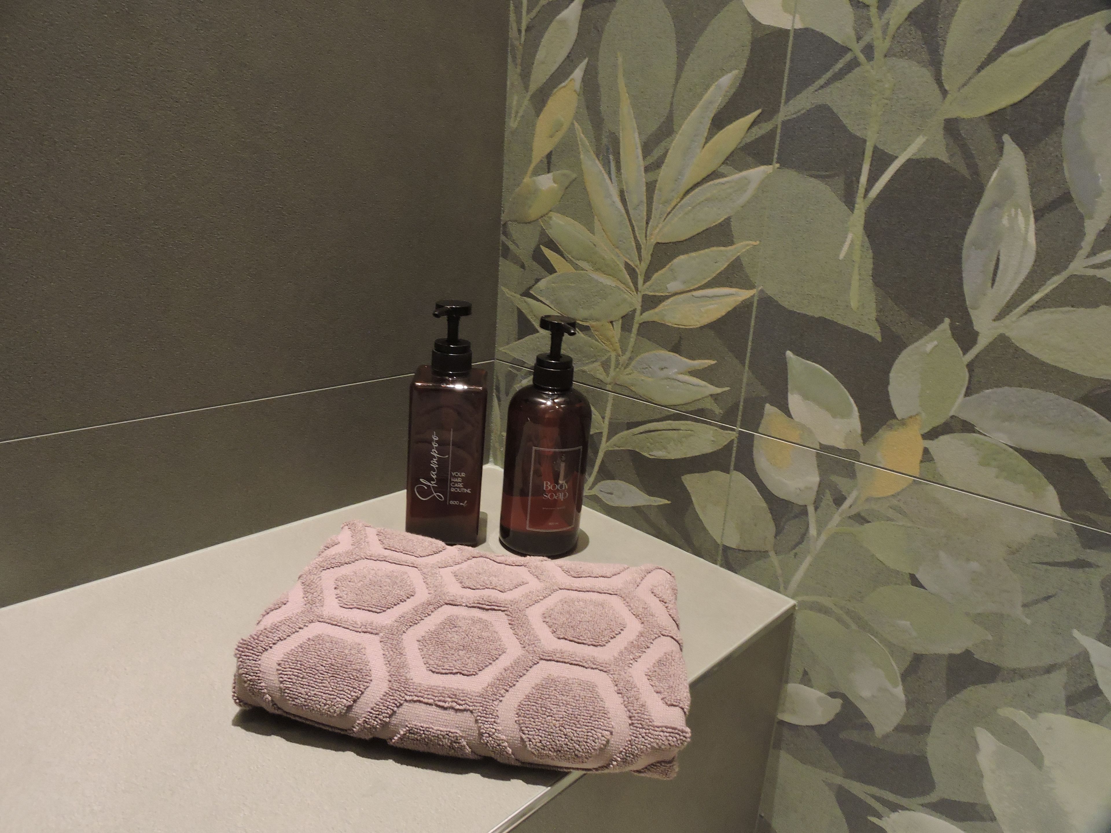 Ein Badezimmer mit einem Handtuch auf einer Ablage, zwei Shampoo-Flaschen und einer Wand mit Muster.