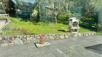 Un mur de pierres avec un banc en pierre et une petite construction en pierre, qui pourrait être un nichoir, dans une zone herbeuse avec des arbres en arrière-plan.