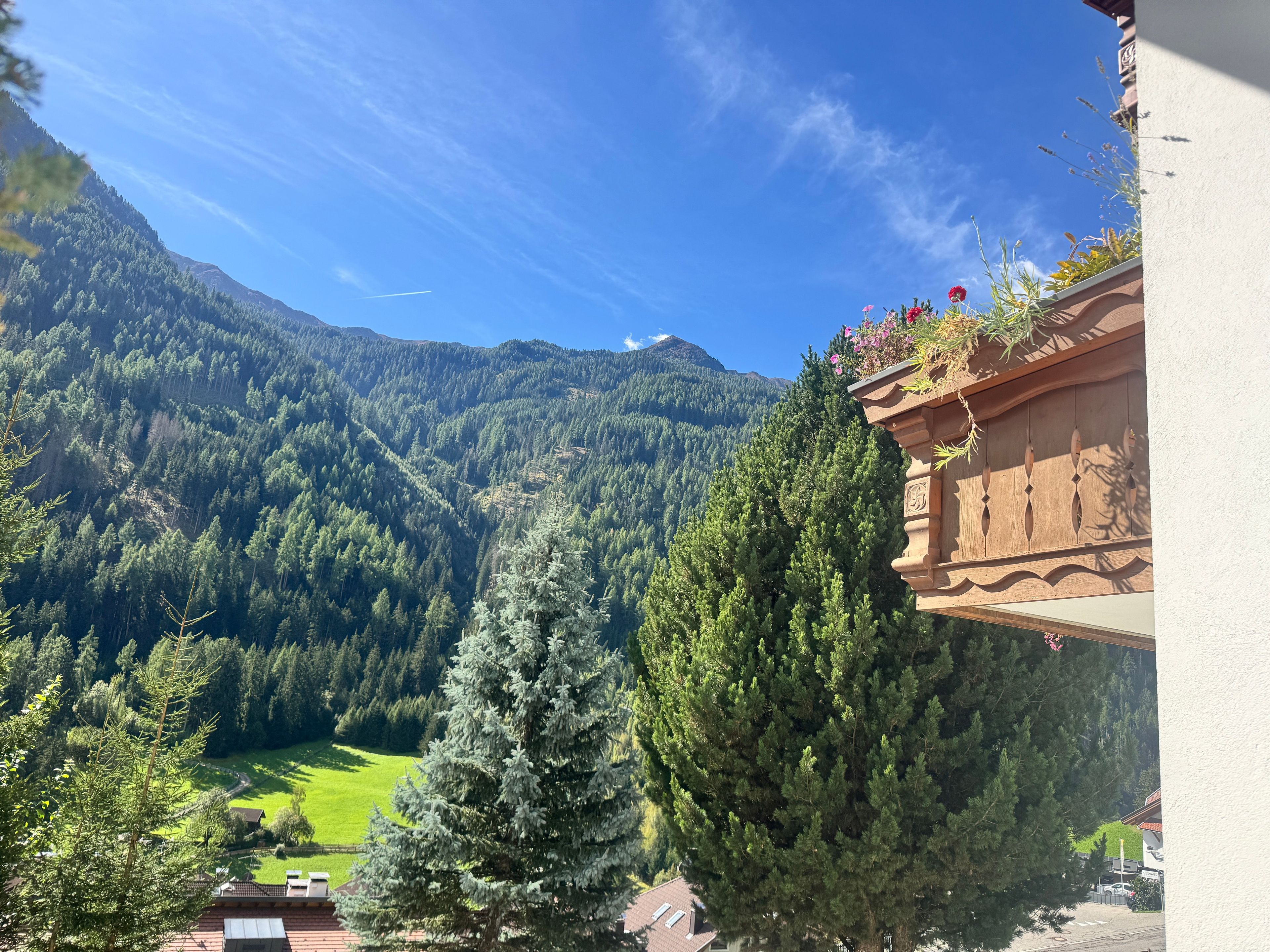 Eine Berglandschaft mit blauem Himmel, einem grünen Tal und einem Gebäude mit einem Balkon, der den Ausblick bietet.