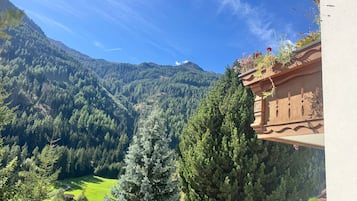 Eine Berglandschaft mit blauem Himmel, einem grünen Tal und einem Gebäude mit einem Balkon, der den Ausblick bietet.