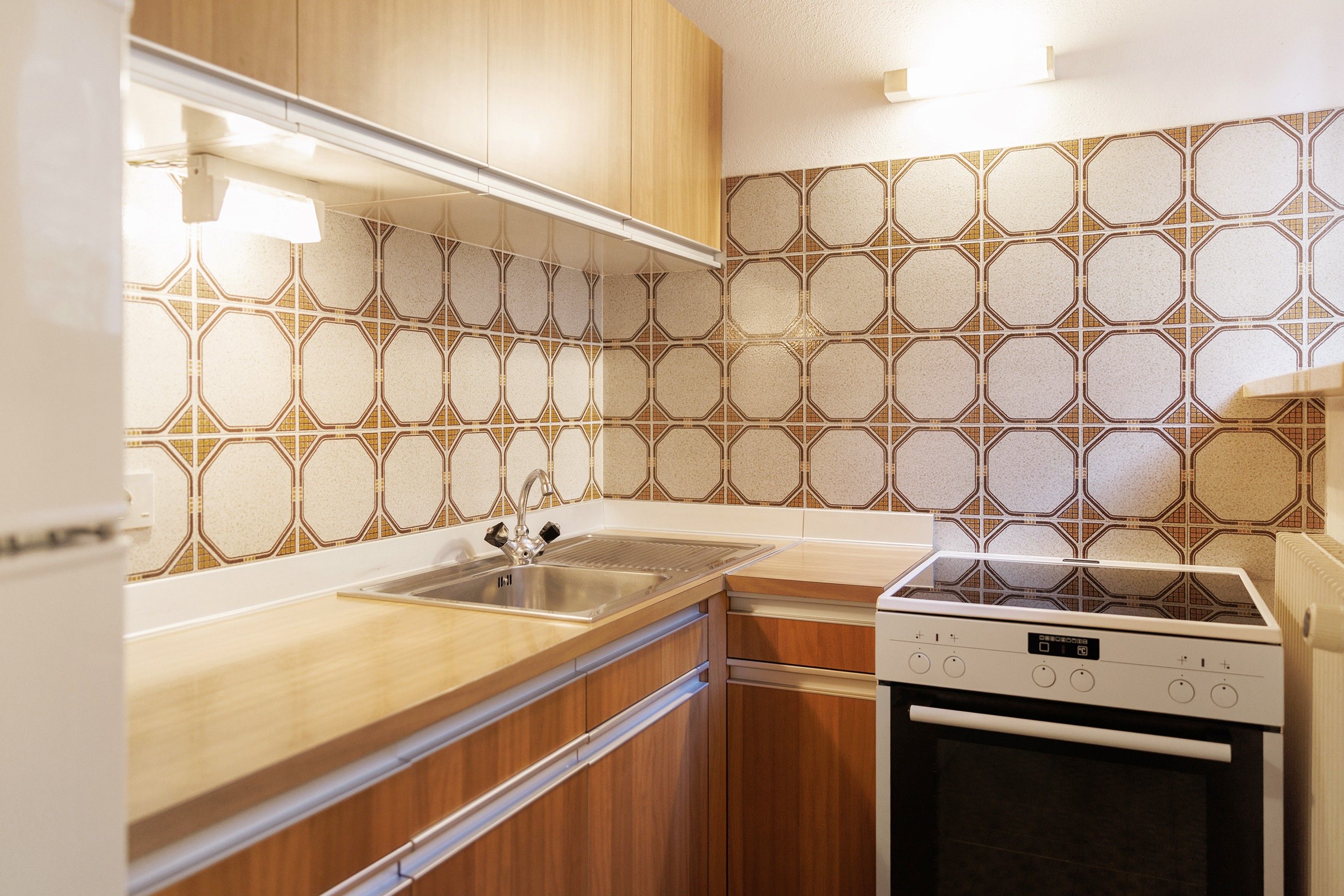 Eine Küche mit Holzausstattung, einem Edelstahlspülbecken, einem Einbauofen und einer Fliesenrückwand mit Muster.