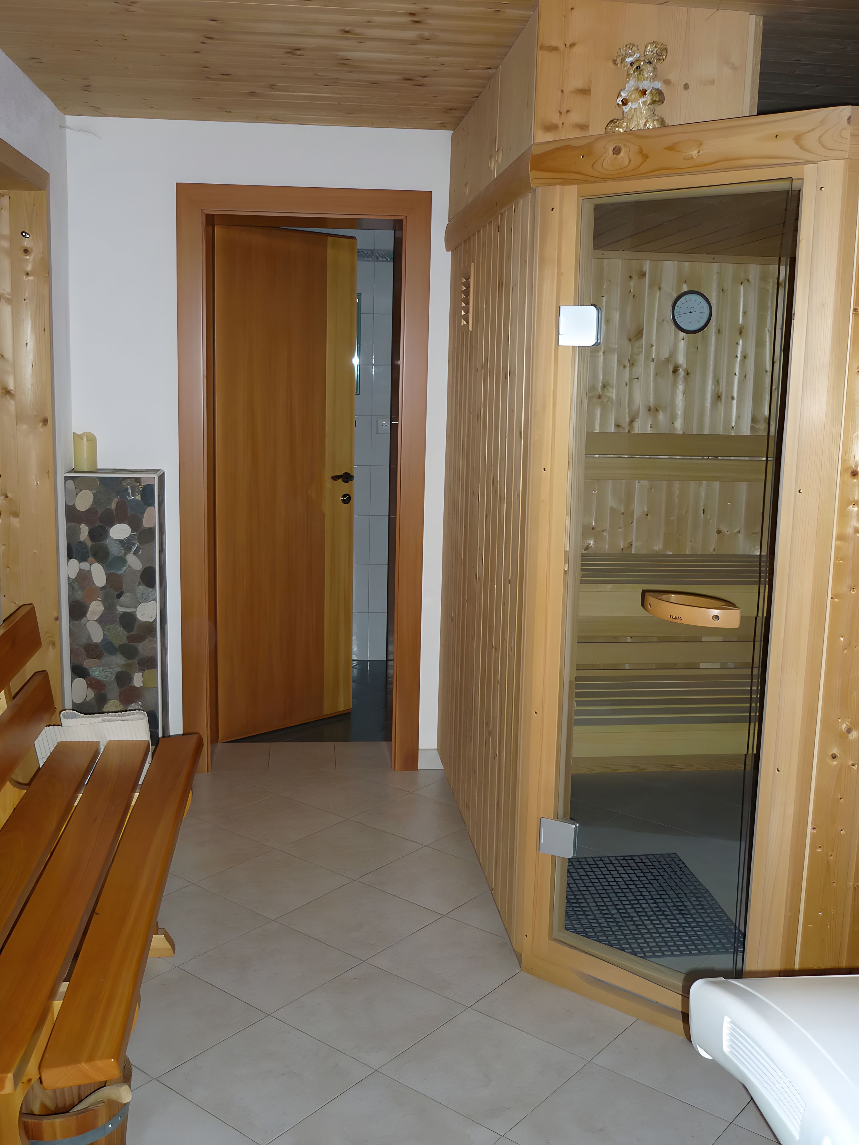 A wooden interior with a bench, a door leading to a tiled room, and a sauna area with a clock.