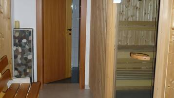 A wooden interior with a bench, a door leading to a tiled room, and a sauna area with a clock.