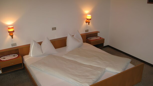 A neatly made bed with a wooden headboard and two bedside tables, each with a lamp. - Apartment '2' with Mountain View, Private Terrace and Wi-Fi (Selva dei Molini)