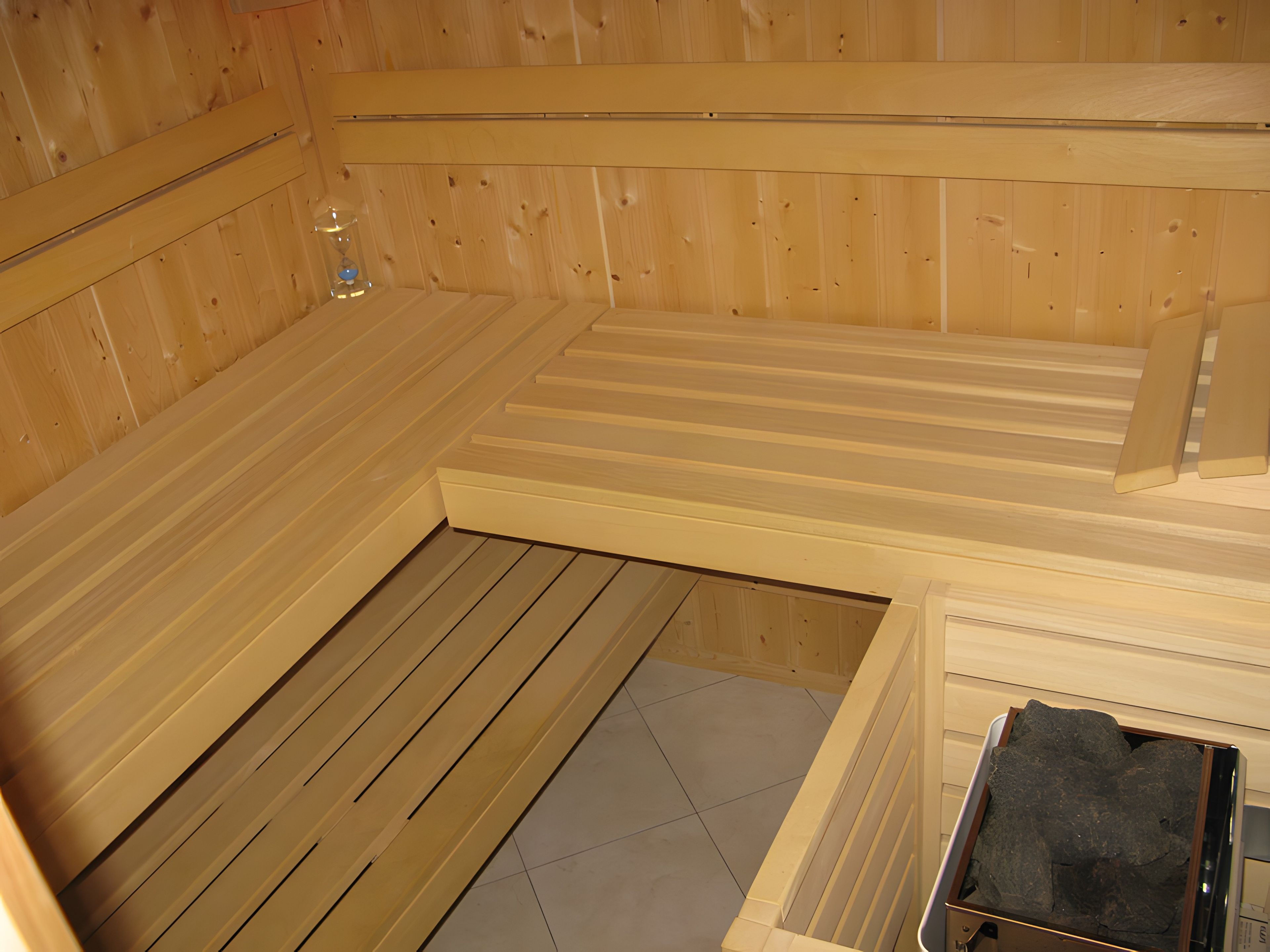 Eine Sauna mit Holzwänden und -bänken, einem gefliesten Boden und einer kleinen Spüle.