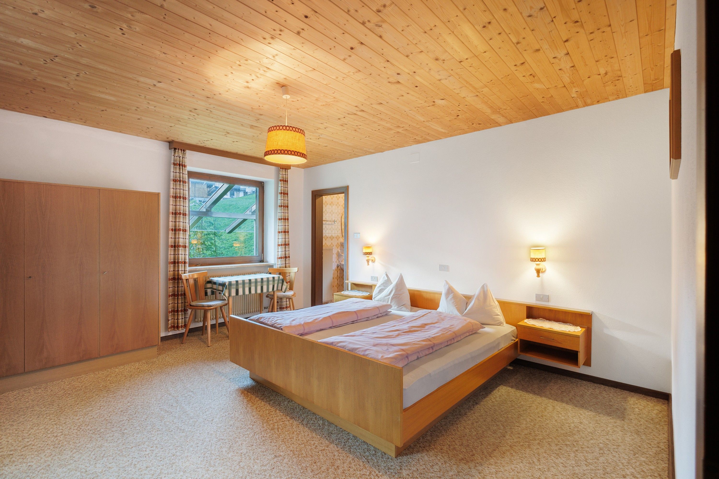 Une chambre avec un plafond en bois, un grand lit, un bureau avec une chaise et deux lampes de chevet.