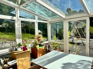 Une véranda dotée d’un toit en verre, d’une table en bois et de diverses plantes en pot.