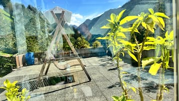 Una stanza con un'ampia finestra vista su un paesaggio montuoso, un'altalena di legno e una botte blu.