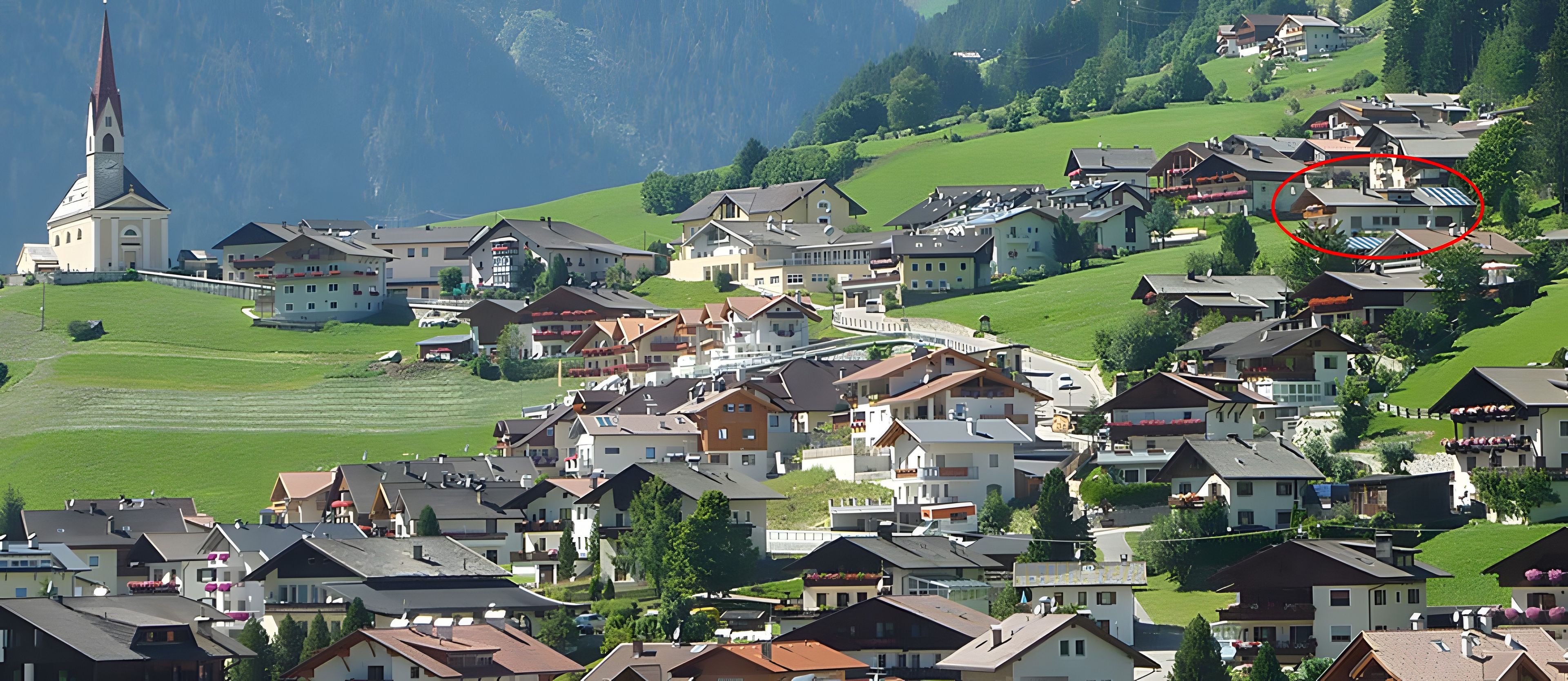 Ein Dorf an einem Hang mit traditionellen Häusern, einer Kirche und einem Berg im Hintergrund.