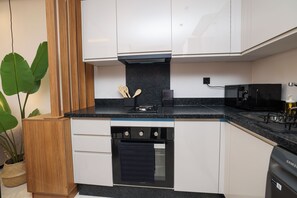 A compact kitchen with white cabinetry, a black countertop, and a stainless steel range hood. - Stylish 1BR apartment in central Casablanca with Terrace & Parking (Dar-el-Beida)