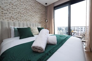 A hotel room with a large bed, a view of the city through a balcony, and a patterned wallpaper. - Stylish 1BR apartment in central Casablanca with Terrace & Parking (Dar-el-Beida)