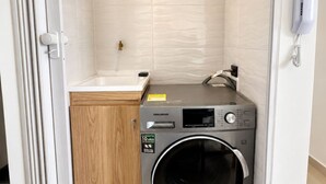 Een kleine wasruimte met een wasmachine, een wasbak en een telefoon.