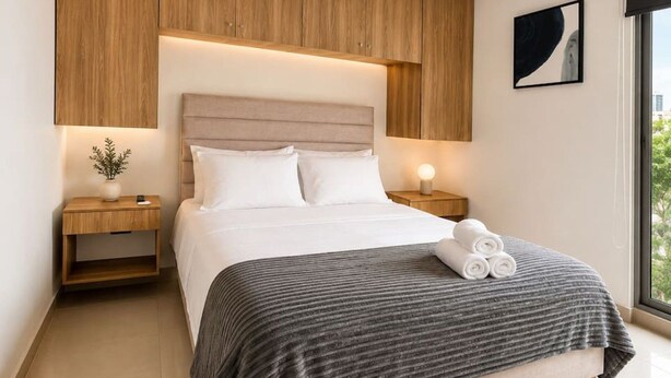 Een moderne slaapkamer met een groot bed, een houten hoofdbord, nachtkastjes met lampen en een raam met uitzicht.