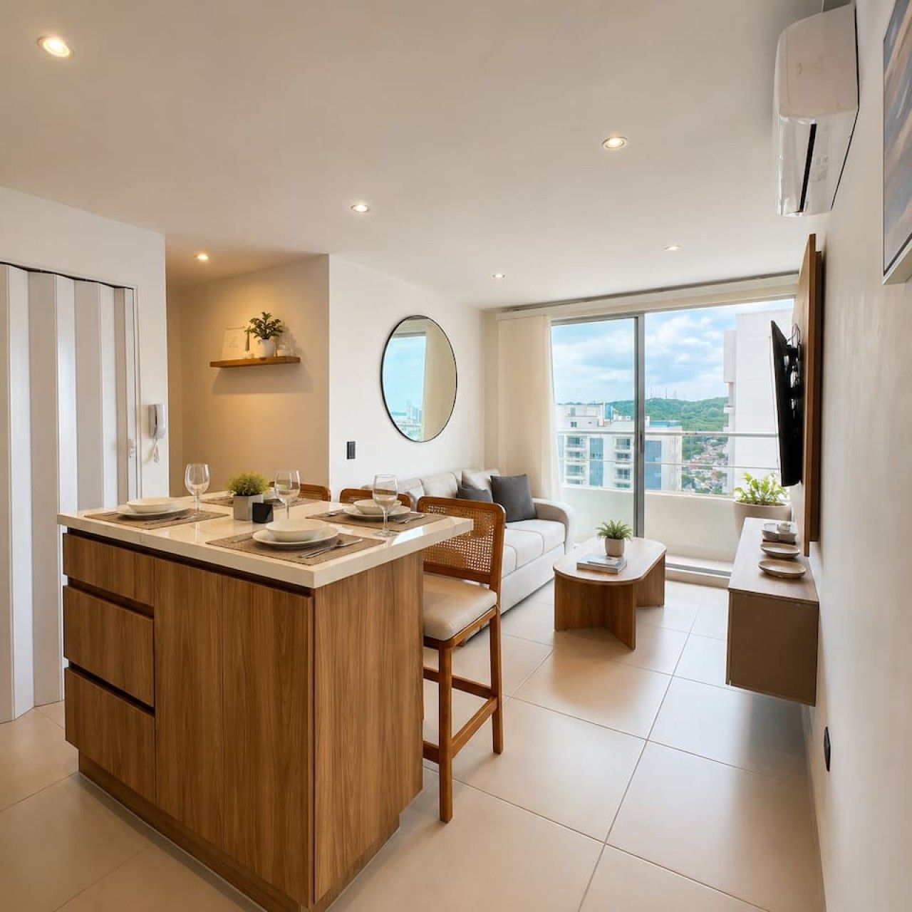 Un apartamento moderno con una isla de cocina, zona de comedor, sala de estar con sofá y balcón con vistas a la ciudad.