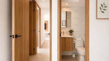 A hallway leading to a bathroom with a toilet, sink, and mirror.