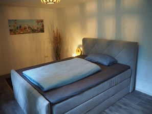 Un dormitorio con una cama, un cuadro en la pared y una lámpara de noche.