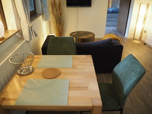Una mesa de madera para comer con una cesta metálica, dos individuales y un posavasos de corcho.