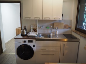 A compact kitchen with a washing machine, a kettle, a sink, and a book on the counter. - Cozy garden studio centrally located near the Kronberg train station (Kronberg im Taunus)