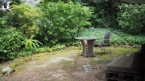 An outdoor seating area with a round table and two chairs, surrounded by lush greenery and a stone pathway. - Cozy garden studio centrally located near the Kronberg train station (Kronberg im Taunus)