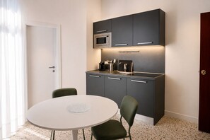 A compact kitchen with a microwave, coffee maker, and cabinets, a round table with two chairs, and a door to the left. - Don Filippo Luxury Home - Vesuvia (Naples)