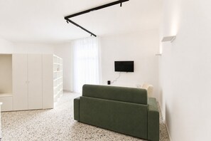 Ein modernes Wohnzimmer mit einem grünen Sofa, weißen Regalen, einem Flachbildfernseher und einem weißen Kleiderschrank.