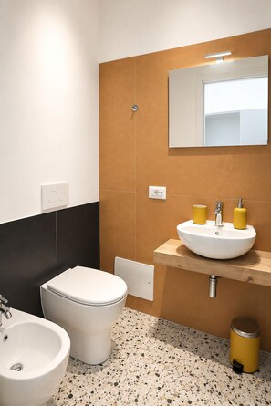 Et moderne badeværelse med et hvidt toilet, en hvid vask og et spejl over vasken.