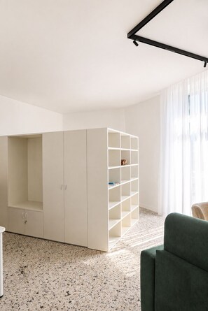 A room with a white wardrobe, a shelving unit, a green sofa, and a speckled floor. - Don Filippo Luxury Home - Riviera (Naples)
