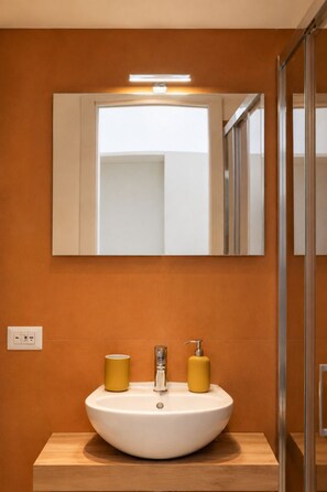 Ein Badezimmer mit einem weißen Waschbecken, zwei gelben Seifenspendern, einem Spiegel und einer Lampe darüber.