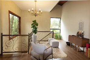 A spacious living area with a staircase, a chandelier, a potted plant, and a view through the window. - House by the dam in Juiz de Fora | pool and nature (Juiz de Fora)
