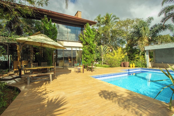 Una casa moderna con un invernadero de vidrio, una terraza de madera y una piscina.