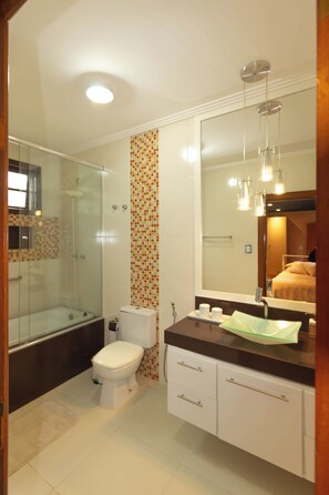 Un baño moderno con cabina de ducha de vidrio, inodoro, tocador con espejo y lavamanos.