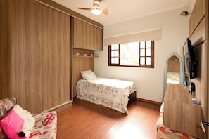 Un dormitorio con cama, armario, ventana y televisión.