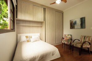 A bedroom with a bed, a wardrobe, a ceiling fan, and two chairs.