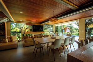 A spacious living area with a large wooden ceiling, a flat-screen TV mounted on the wall, and a dining table surrounded by chairs.