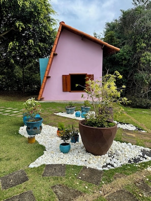 A pink building with a sloped roof, surrounded by a garden with various potted plants and a gravel pathway. - House by the dam in Juiz de Fora | pool and nature (Juiz de Fora)