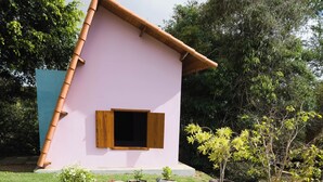 Ein Haus mit rosa Fassade und braunem Dach, umgeben von einem Garten mit verschiedenen Kübelpflanzen und einem weißen Kiesweg.