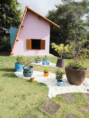 Una casa de fachada rosa y techo marrón, rodeada de un jardín con diversas macetas y un camino de grava blanca.