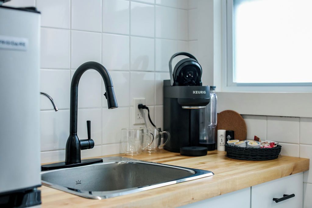 Una cocina moderna con una cafetera negra, un lavamanos de acero inoxidable y una encimera de madera.