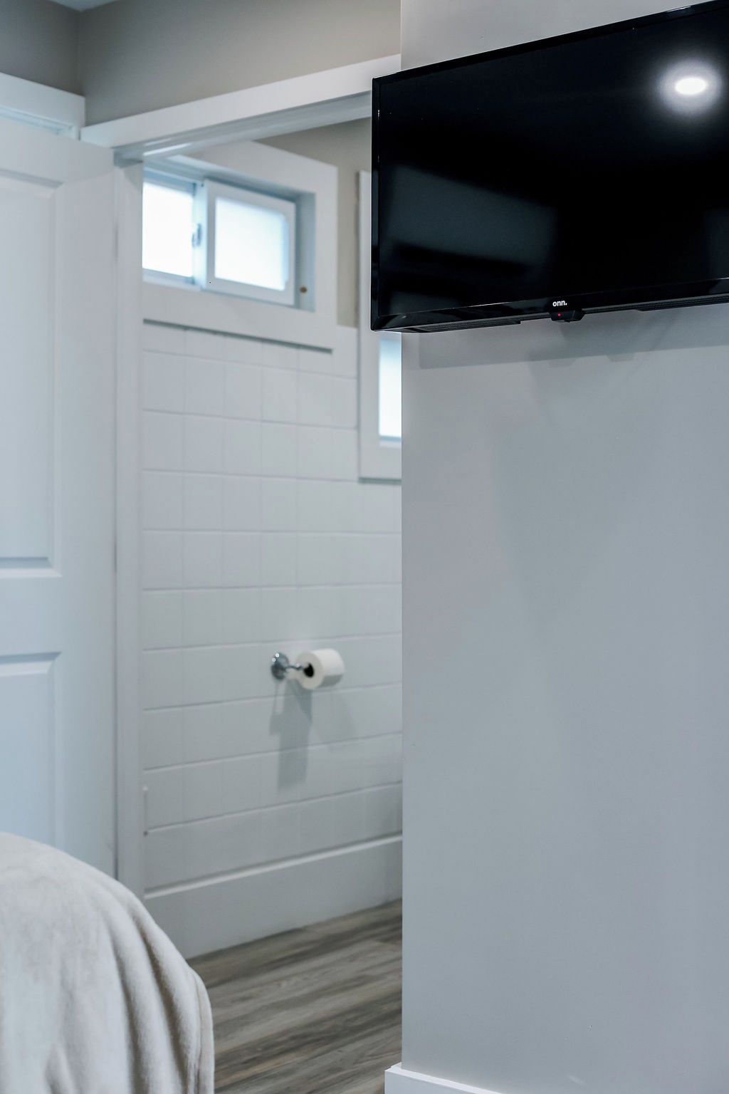 A room with a white door, a toilet paper holder, and a black television mounted on the wall.