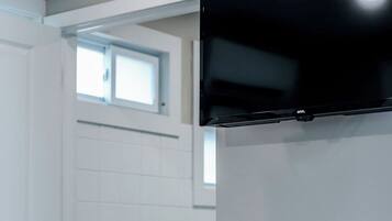 A room with a white door, a toilet paper holder, and a black television mounted on the wall.