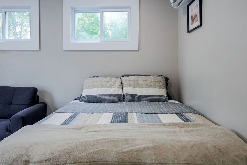 A bedroom with a bed, a chair, and two windows.