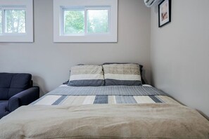 A bedroom with a bed, a chair, and two windows.