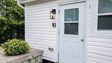Une maison blanche avec le numéro « 10 » sur la porte, un petit porche avec un jardinière et une fenêtre munie d’un moustiquaire.