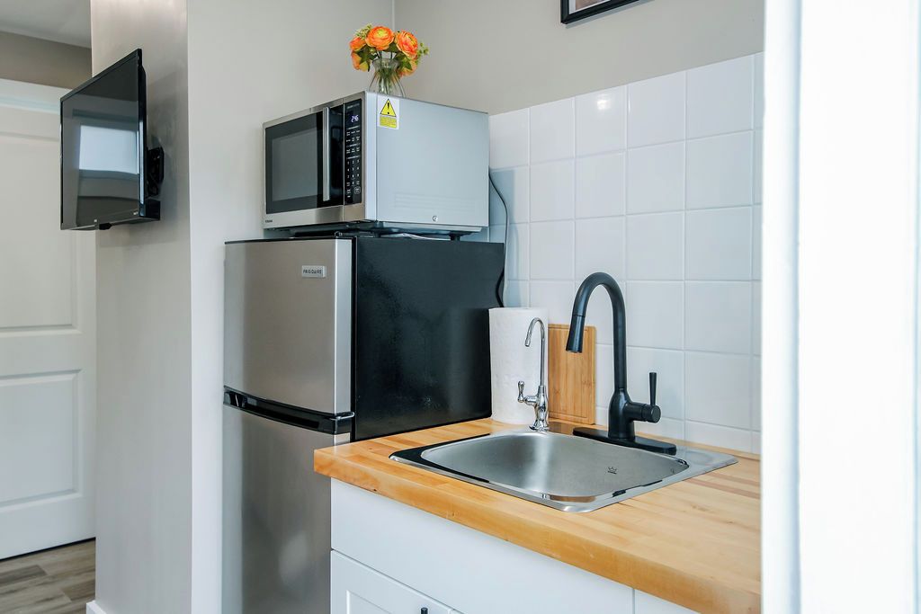 A modern kitchen with a stainless steel refrigerator, a microwave, and a sink with a wooden countertop.