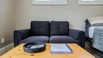 Une pièce avec un canapé gris foncé, une table en bois sur laquelle se trouvent un panier et un carnet, et un lit recouvert d’une couverture à rayures.